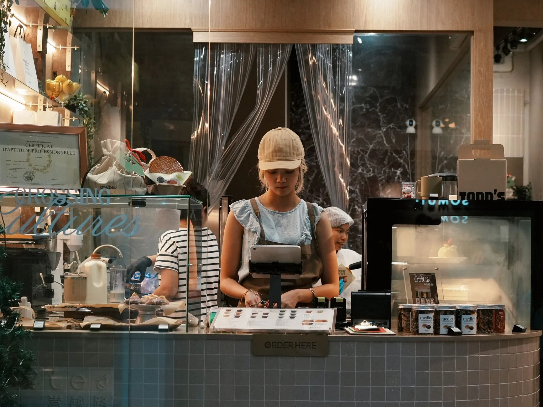 A young woman behind the counter at a modern bakery, engaging with a point of sale system. – Foto: Maxine Xin / Pexels