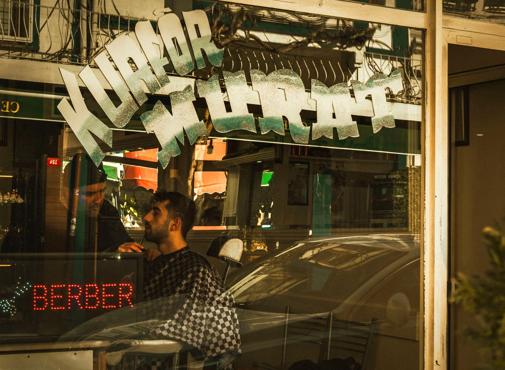 Man getting a haircut in a barbershop with reflective window signage. – Foto: Damla Karaağaçlı / Pexels