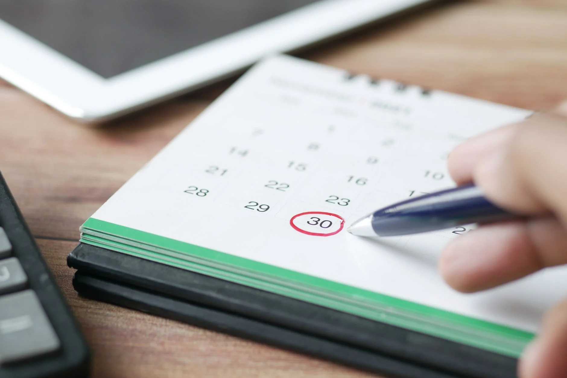 Close-up shot of a hand marking a date on a calendar with a pen, emphasizing planning and scheduling. – Foto: Towfiqu barbhuiya / Pexels