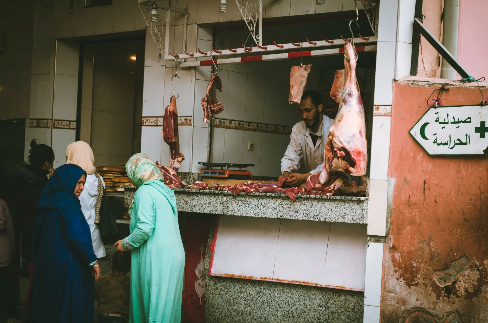 A lively outdoor market scene showing a butcher serving customers at a meat stall. – Foto: Nicolas Postiglioni / Pexels