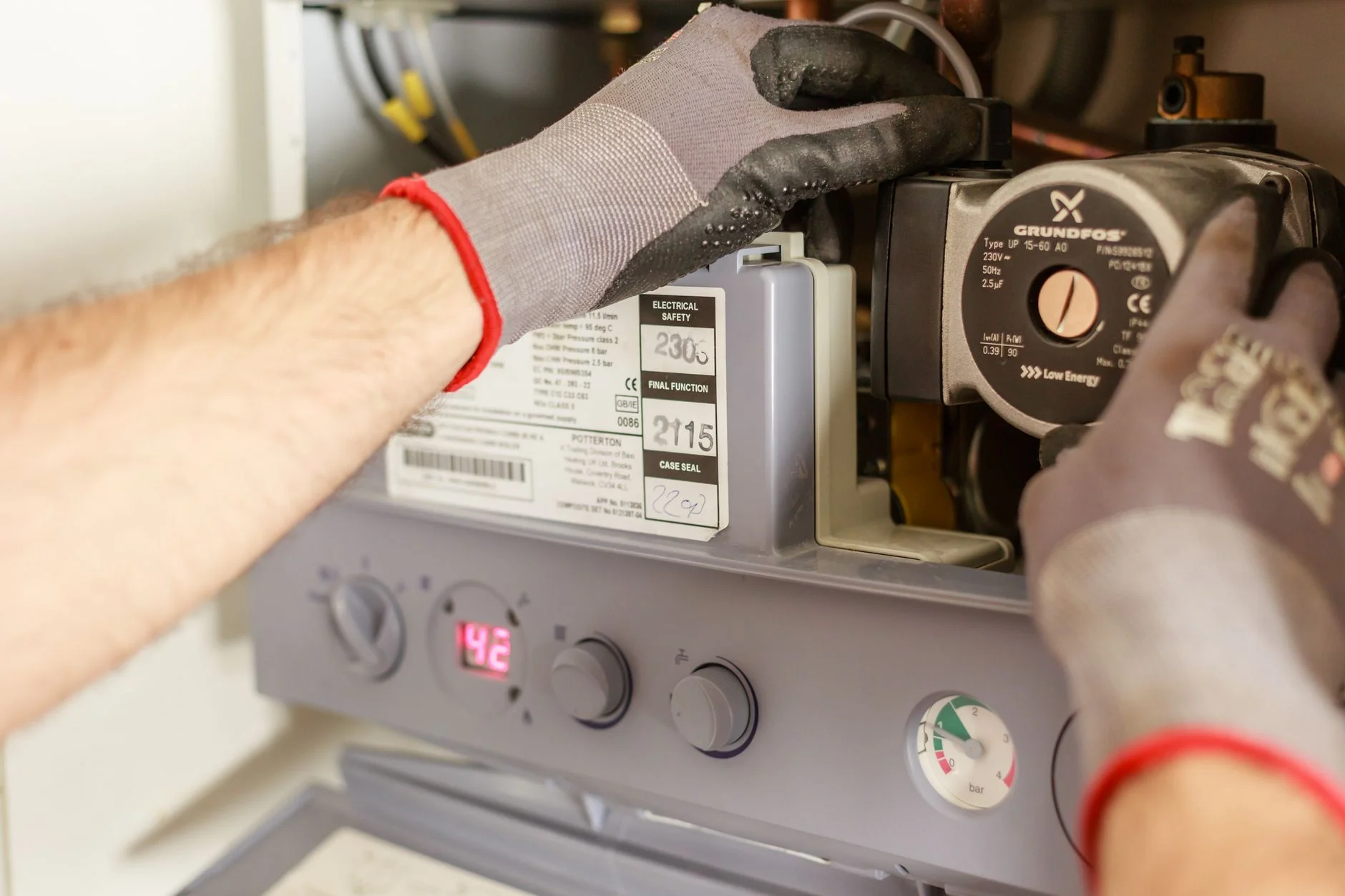 Close-up of hands adjusting a boiler system with precise instrumentation, showing maintenance work. – Foto: Heiko Ruth / Pexels